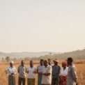 Un groupe de personnes se tient dans un champ aride et sec, tenant une banderole informant sur la rareté des pluies au Sud-Kivu.